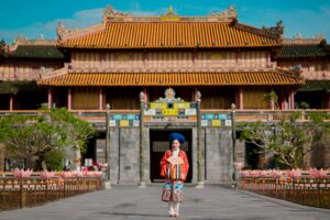 Asian woman in traditional attire stands before Hue Imperial City, Vietnam's historic landmark.