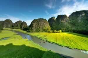 Aerial view of a scenic river cutting through lush green fields with towering limestone mountains under a clear sky.