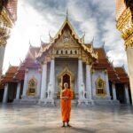 A Buddhist monk standing in front of the iconic Wat Benchamabophit Temple, Bangkok, capturing spiritual tranquility.